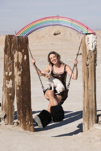 Ashely Norton swinging with dog in lap under rainbow sculpture